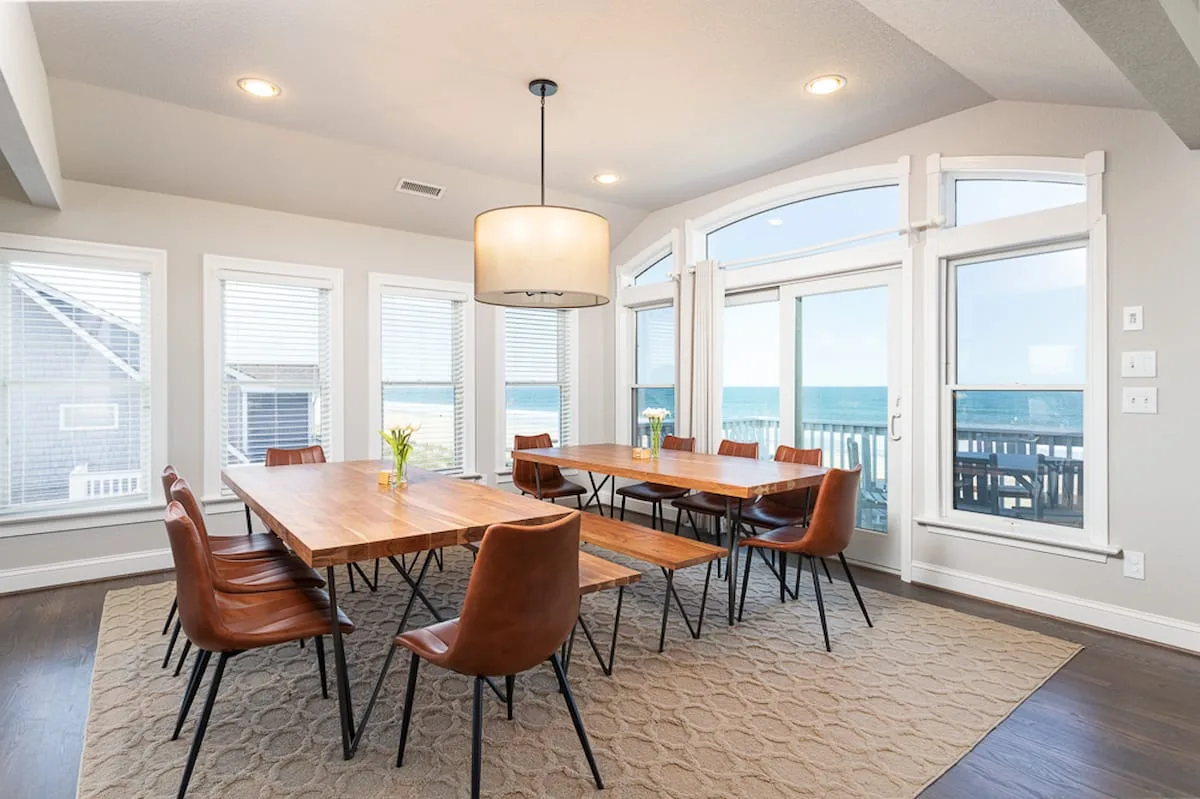 Un comedor con una mesa de madera y sillas junto a grandes ventanas con vistas al agua.