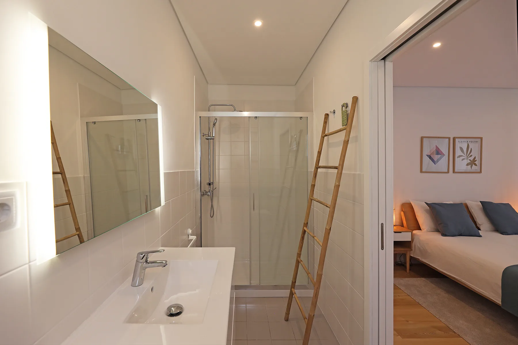 A bright bathroom with a sink and glass shower beside an open bedroom.