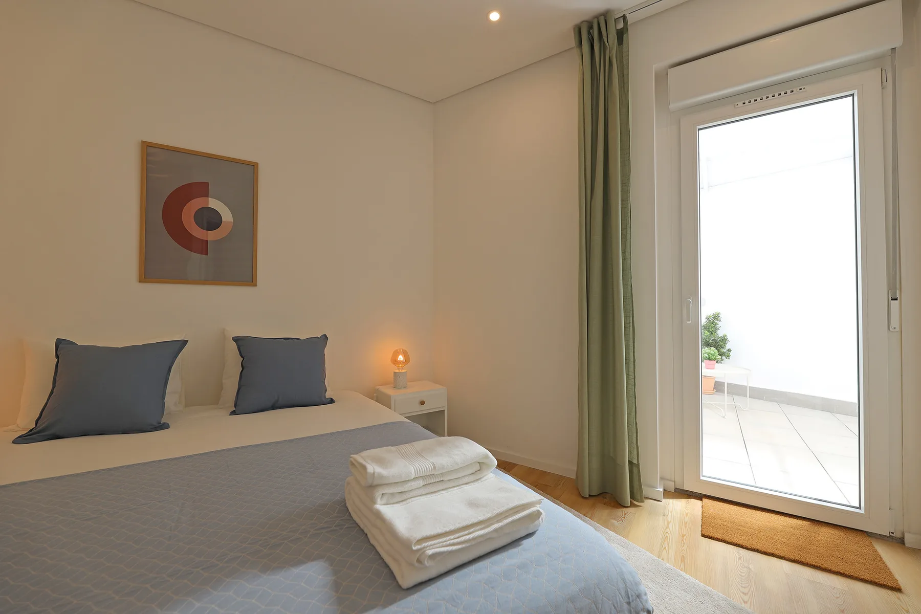 A bedroom with a neatly made bed beside a glass door opening onto a terrace.