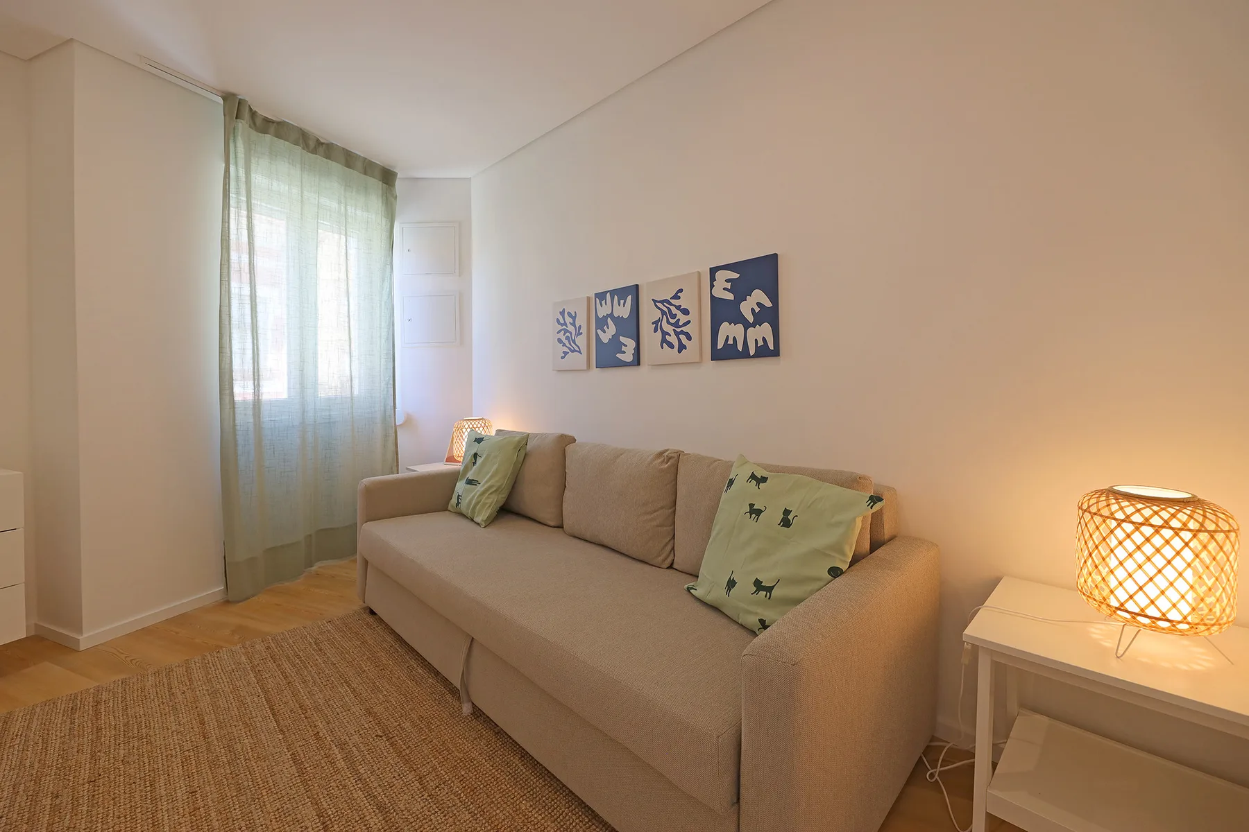 A living room with a beige sofa, a woven rug, and a glowing table lamp.