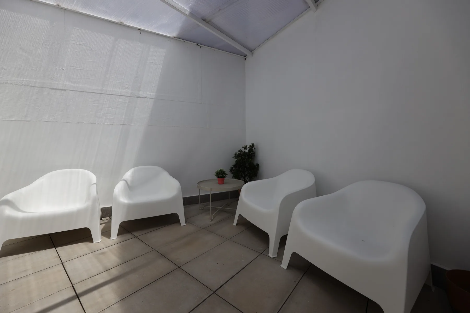 A covered terrace seating area with white chairs and a small potted plant.