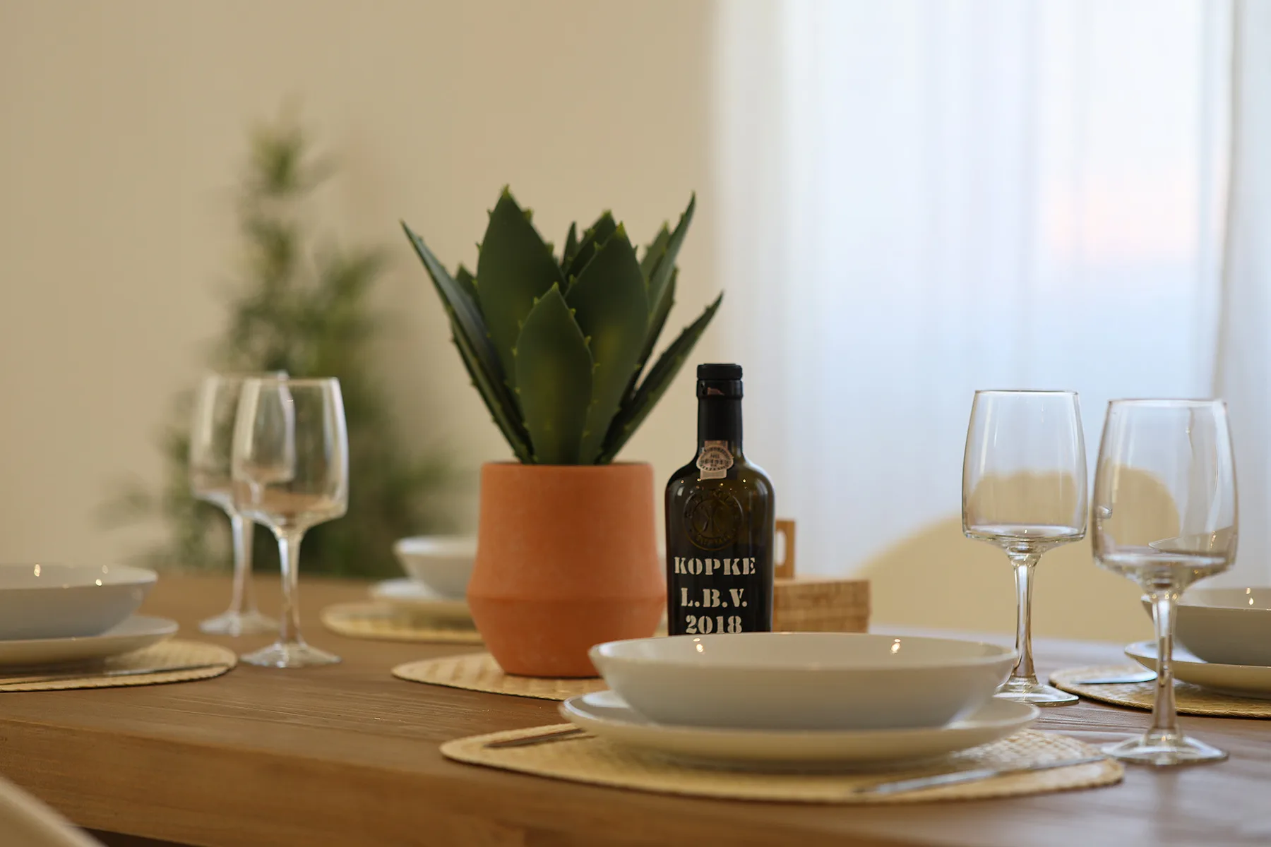 A dining table is set with plates, glasses, and a potted plant.