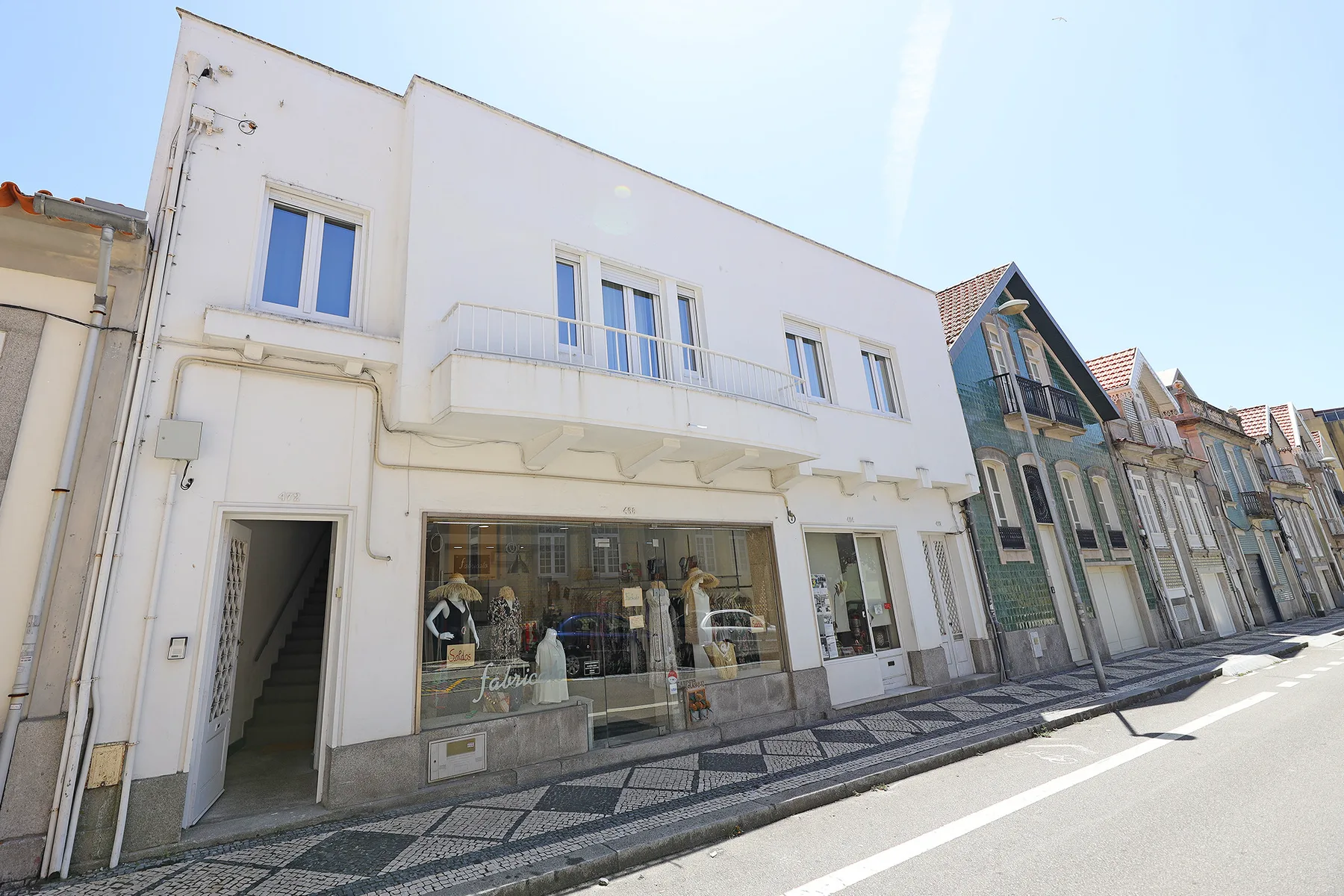 A white multi-story building with storefront windows faces a paved sidewalk.