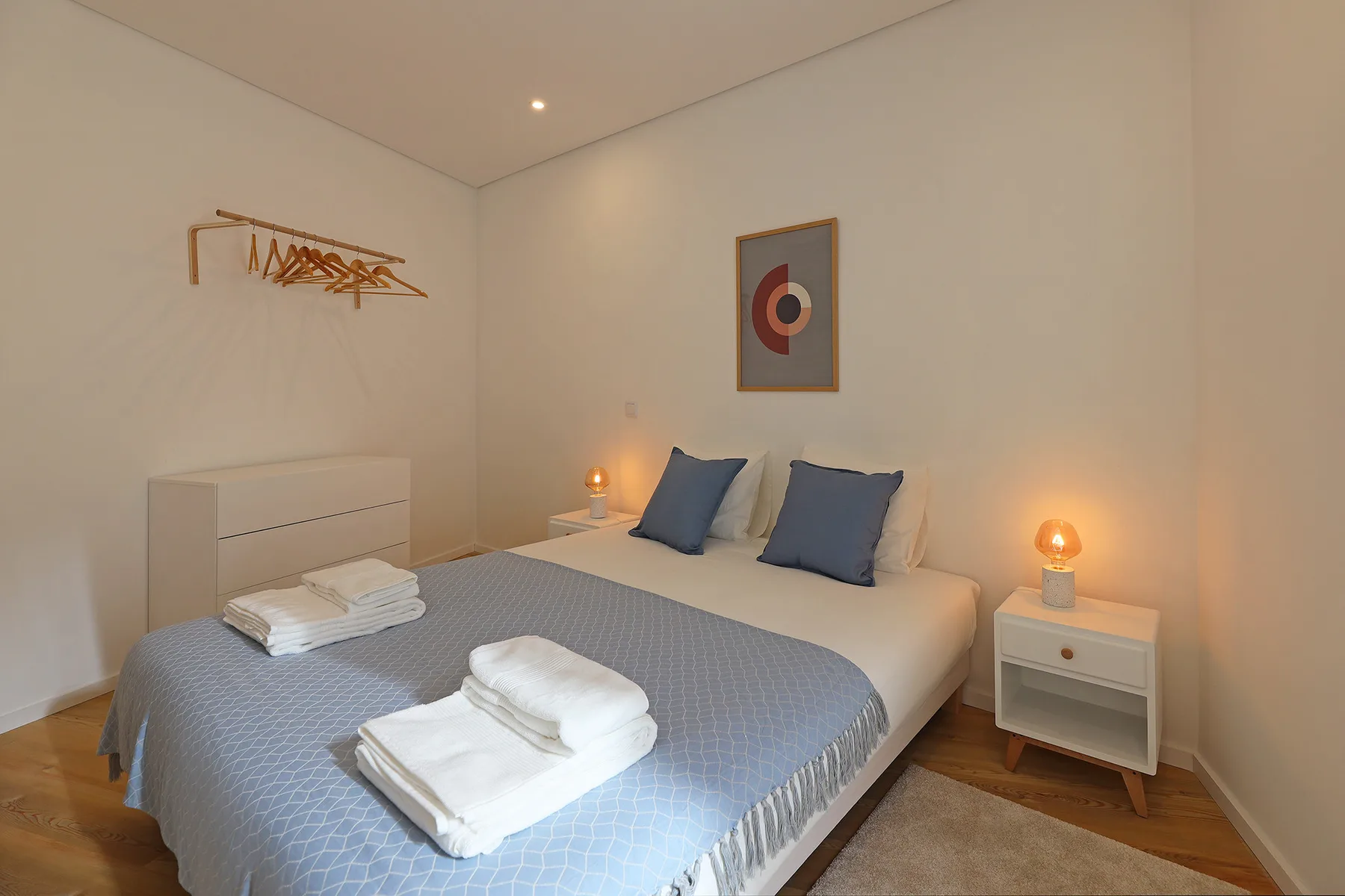 A bedroom with a double bed, folded towels, and bedside lamps.