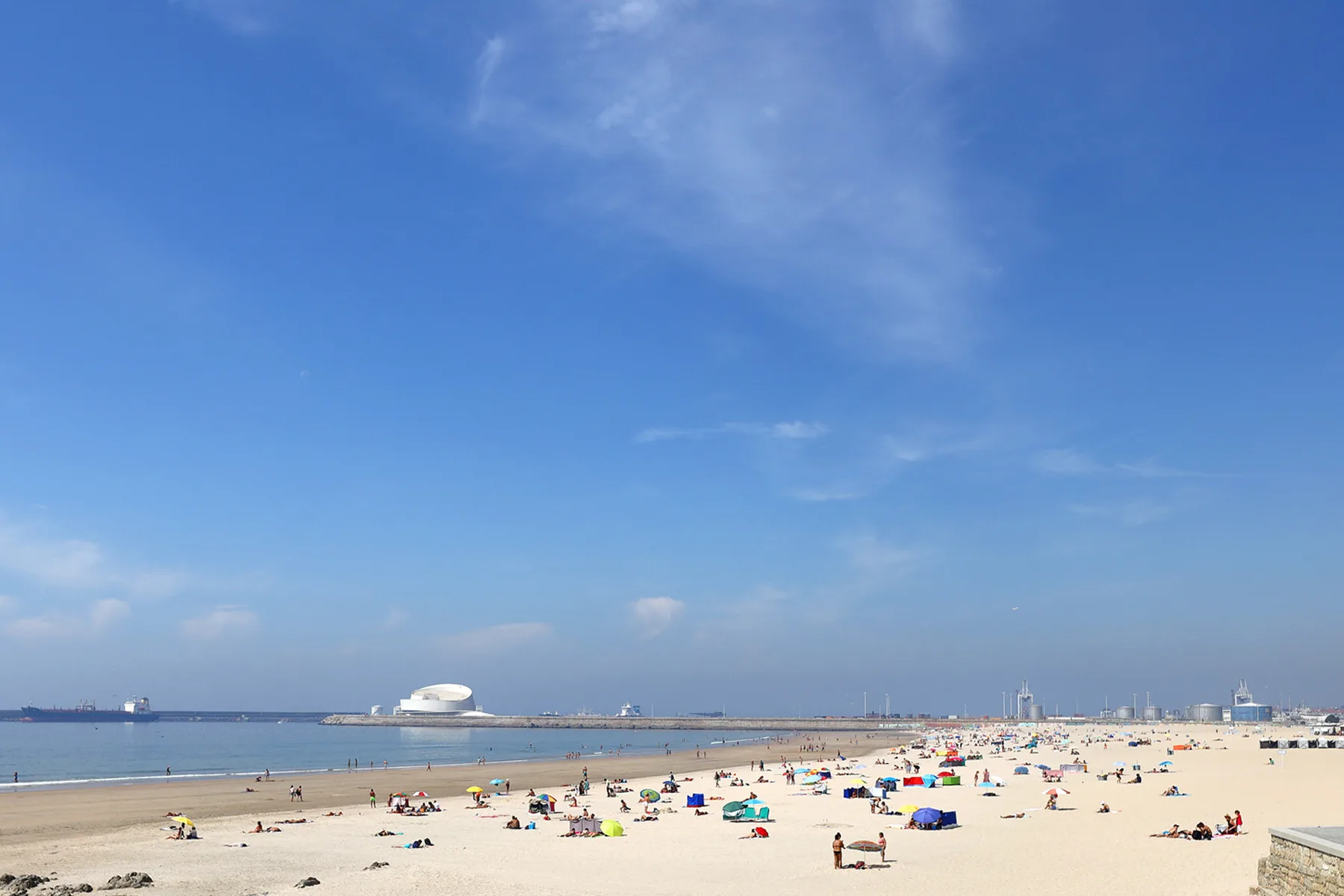 A sandy beach with colorful umbrellas stretches along calm water beneath a blue sky.