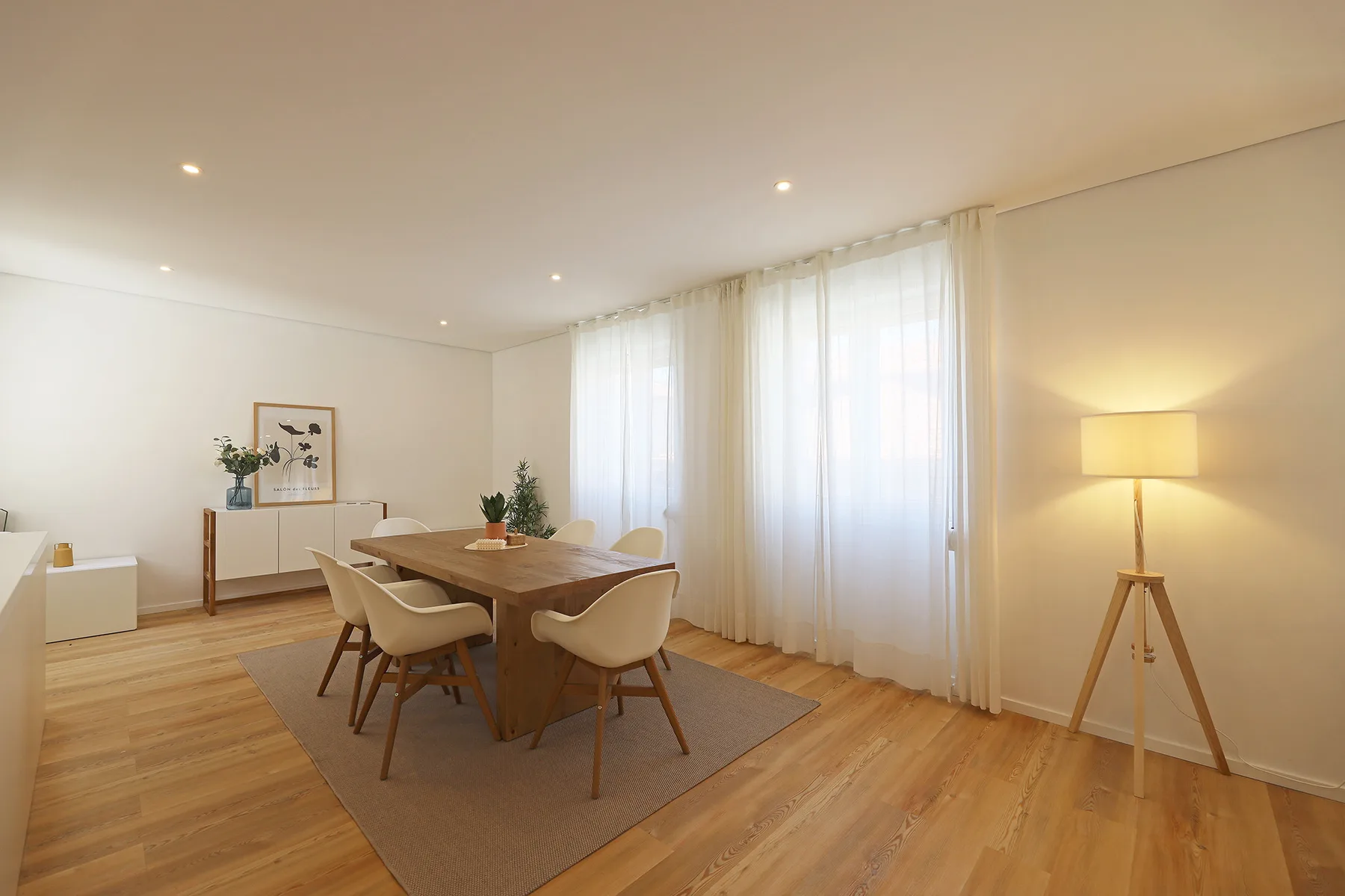 A bright dining area with a wooden table beside tall curtained windows.