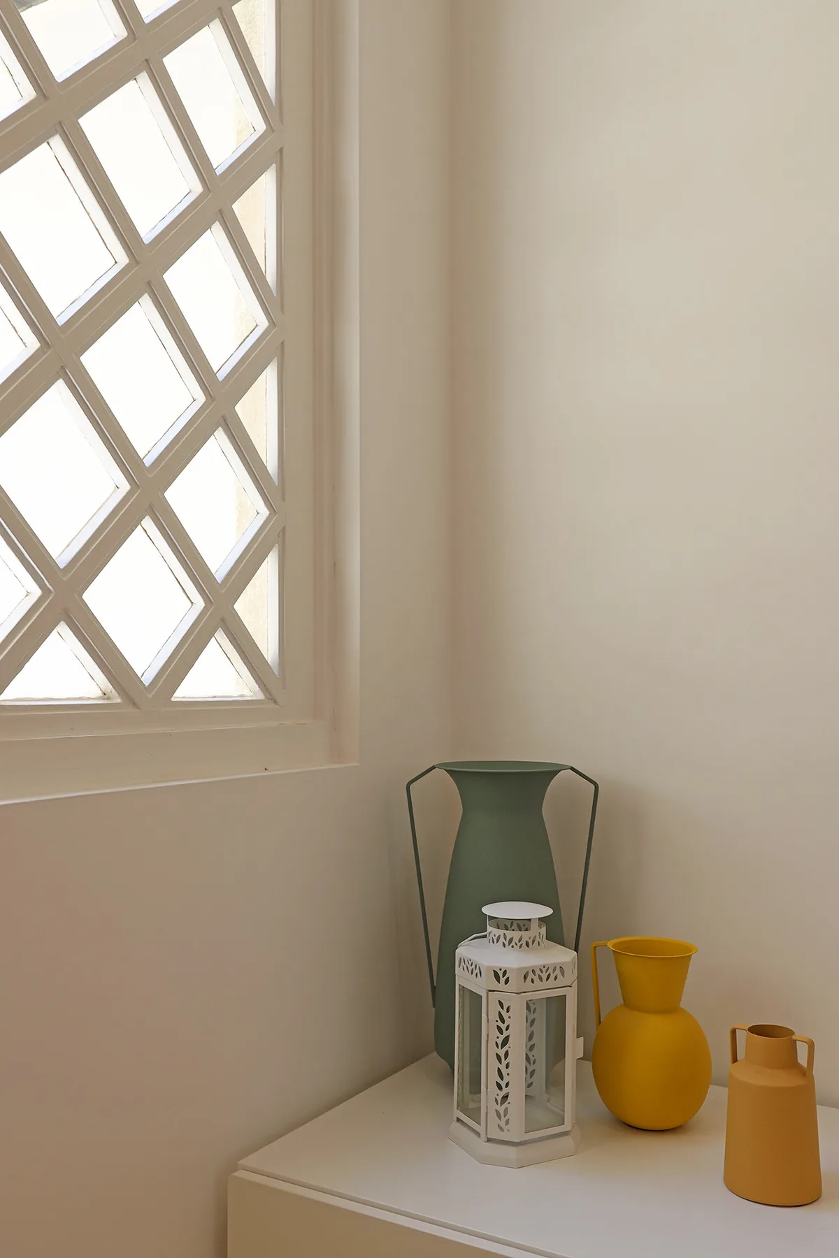 A bright interior corner with a geometric window and decorative vases on a table.