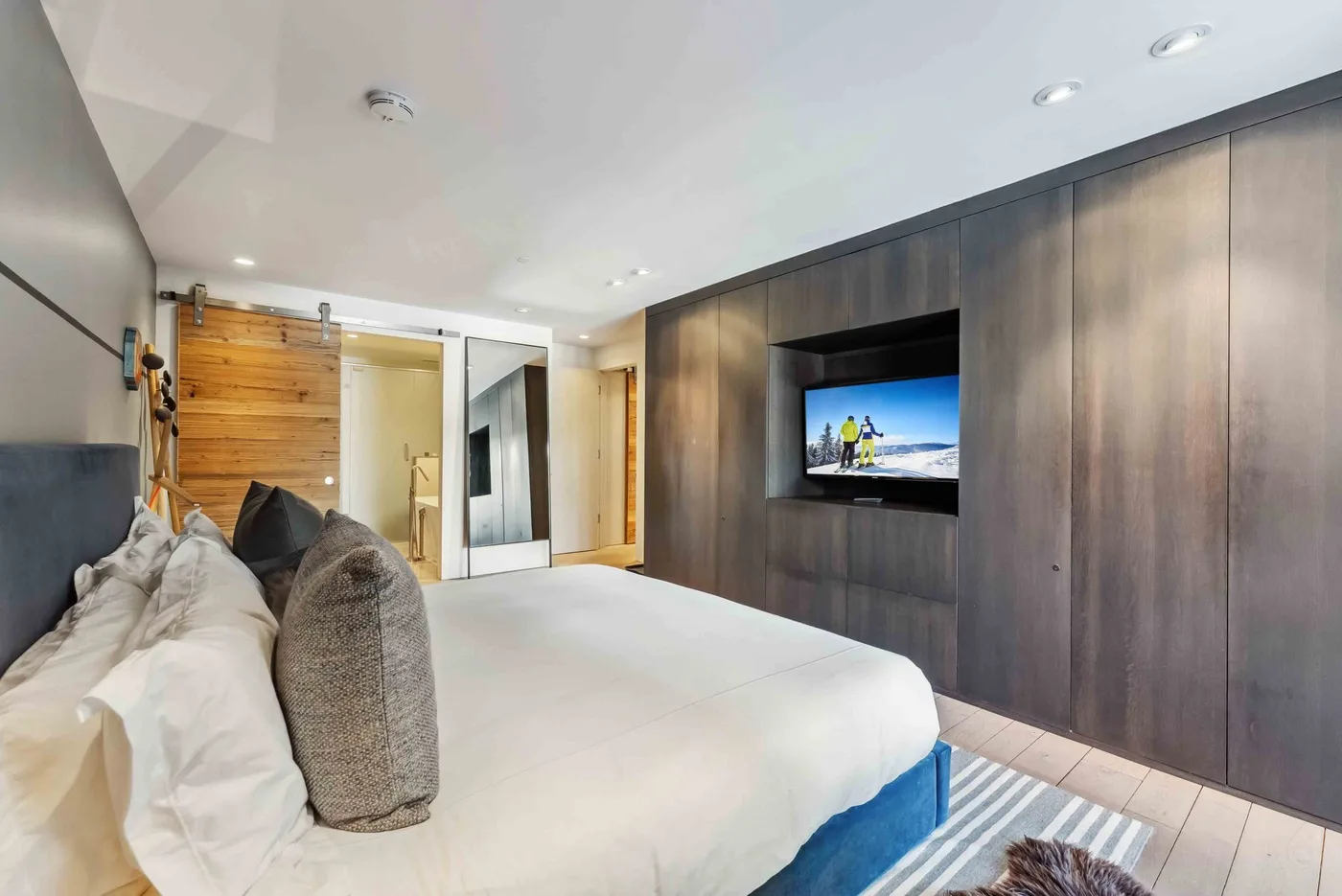 Un dormitorio con una cama grande junto a una pared oscura revestida de madera y un televisor integrado.