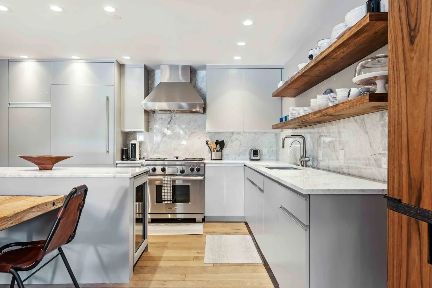 Una cocina moderna con gabinetes blancos, electrodomésticos de acero inoxidable y estantes abiertos de madera.