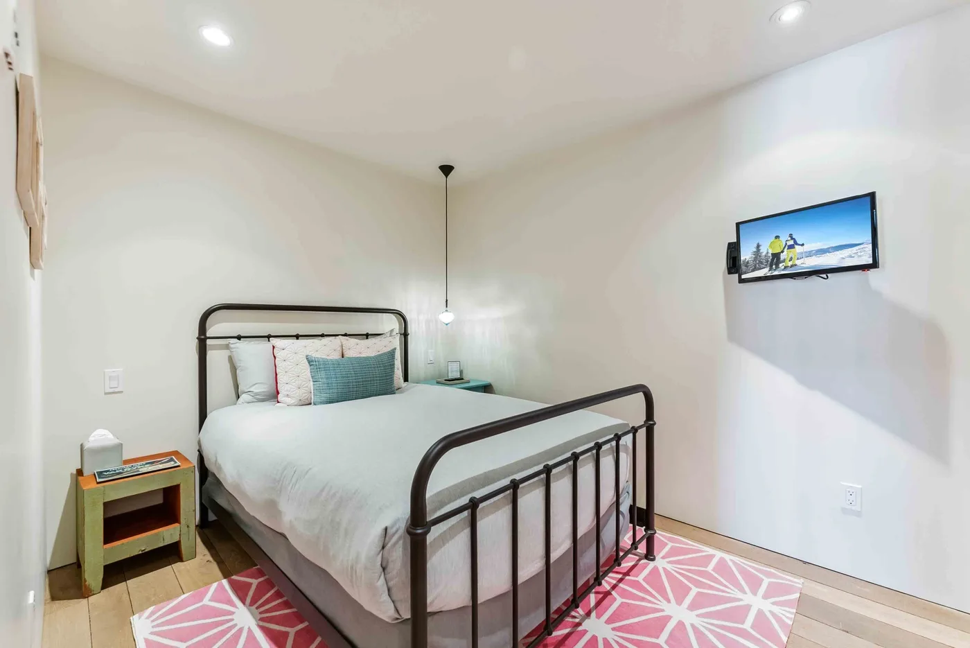 Un dormitorio con una cama de metal, una mesita de noche y un televisor en la pared.