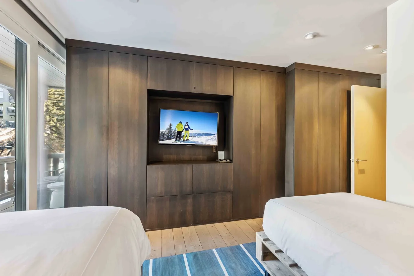 Un dormitorio con dos camas y un televisor empotrado en paneles de madera oscura.