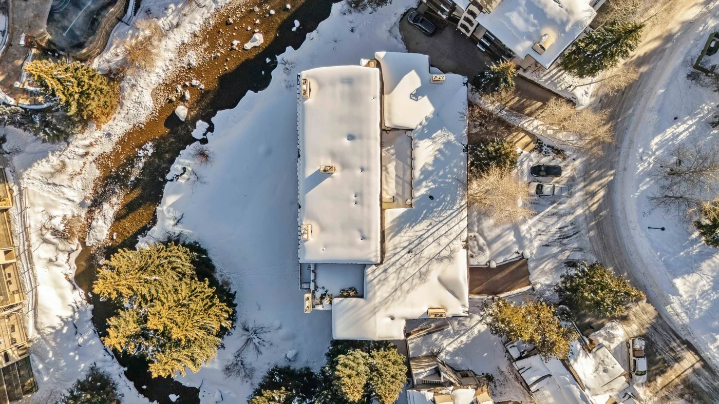 Vista aérea de un edificio cubierto de nieve junto a un arroyo sinuoso.