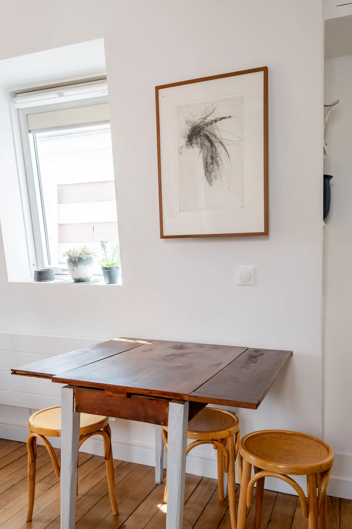 Un comedor con una mesa de madera y taburetes bajo una obra enmarcada.