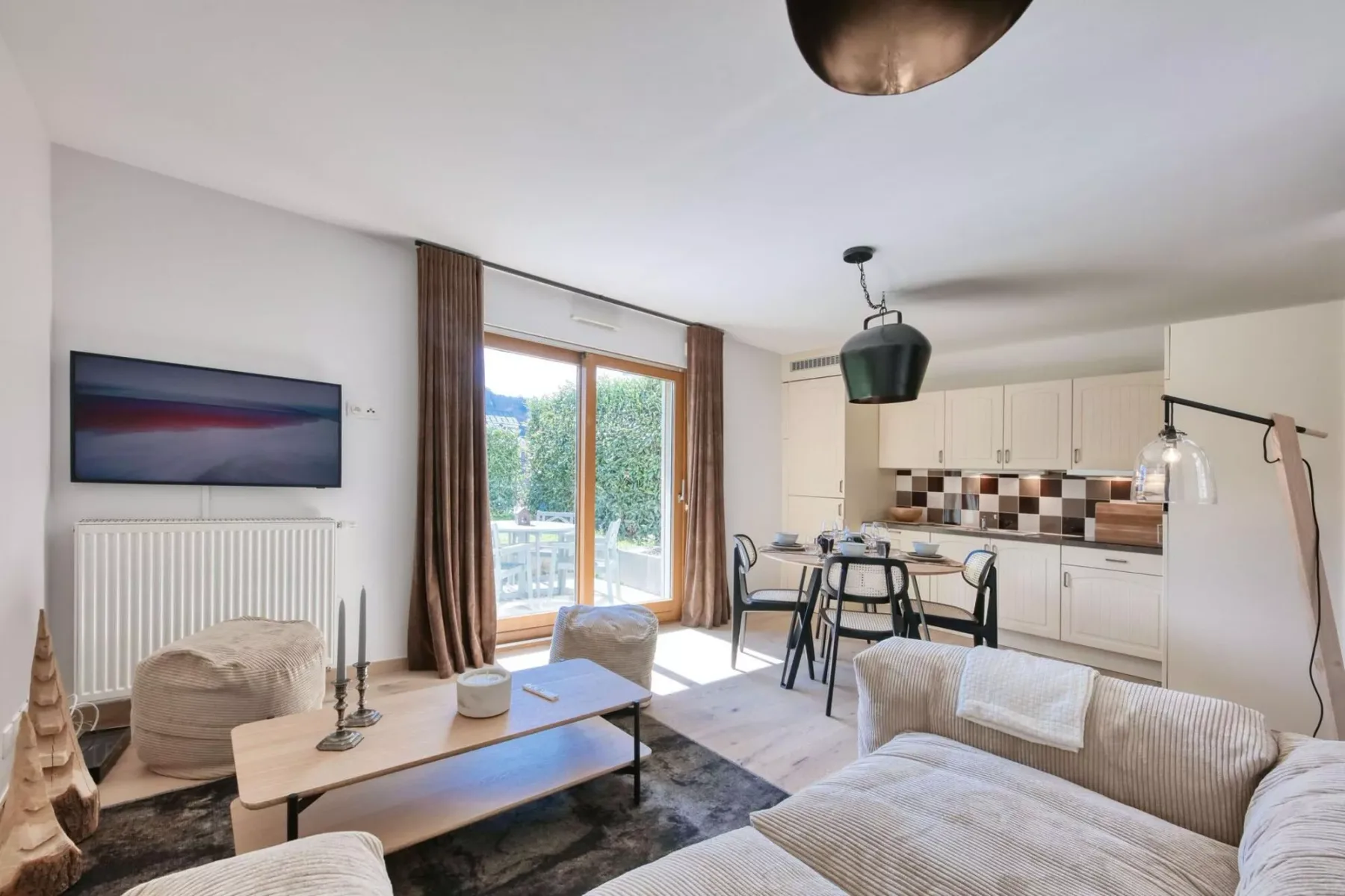 A bright living room opens onto a kitchen, with seating beside large glass doors.