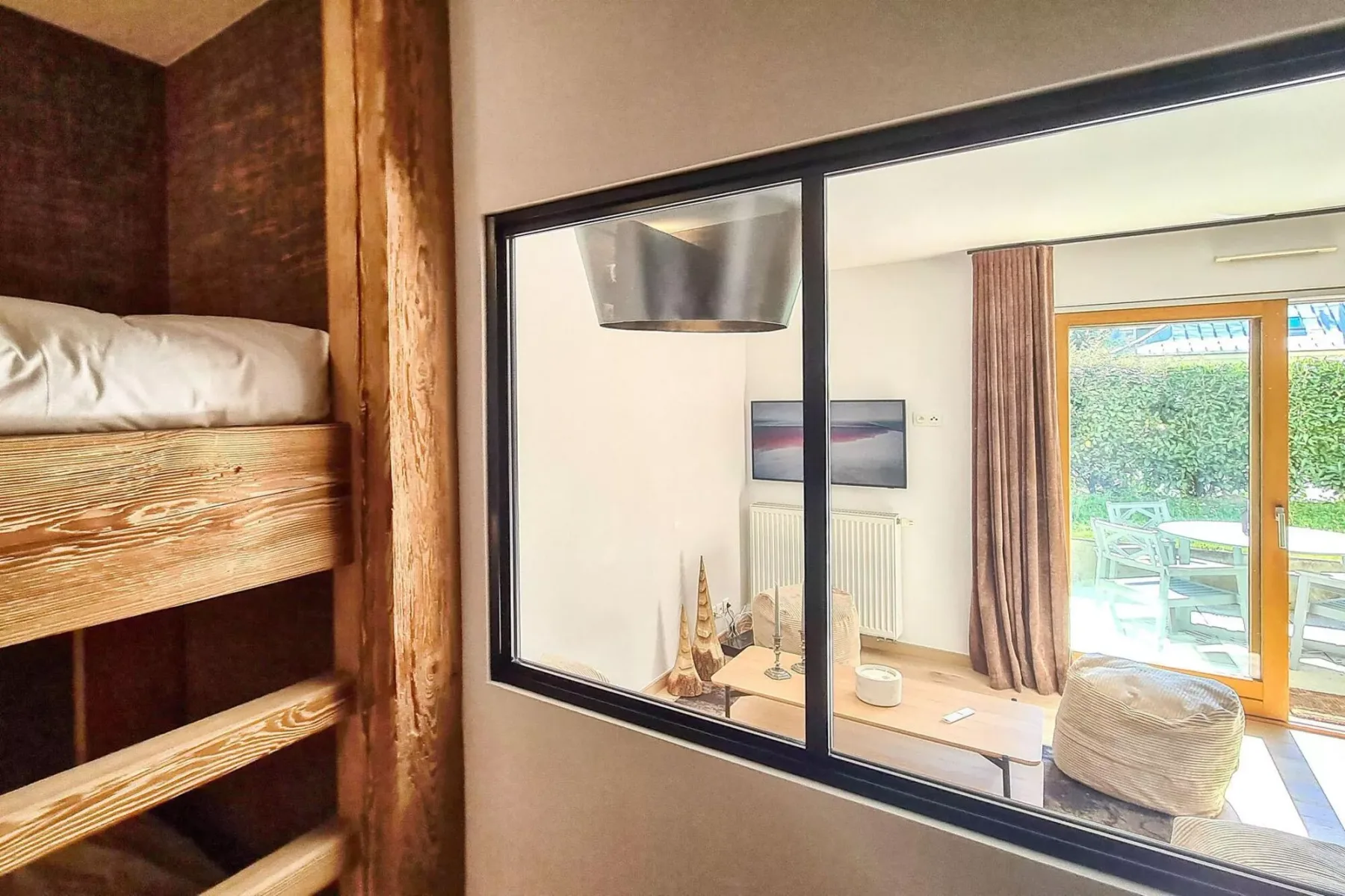 A sleeping area overlooks a bright living space with glass doors opening to greenery.