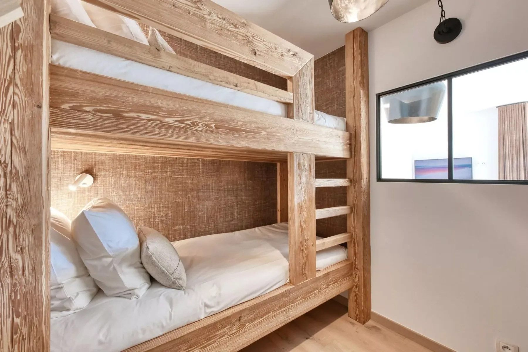 A bunk-bed sleeping area with wooden bunks, white bedding, and a window.
