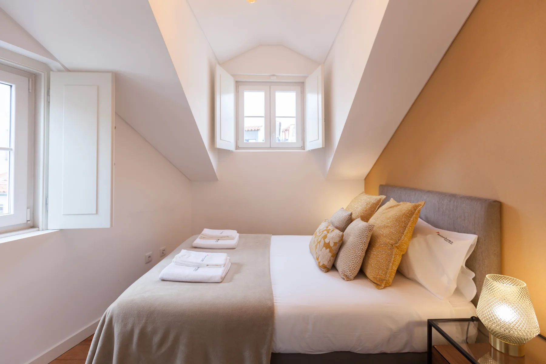 A bright bedroom with a bed and folded towels beneath sloped ceilings.