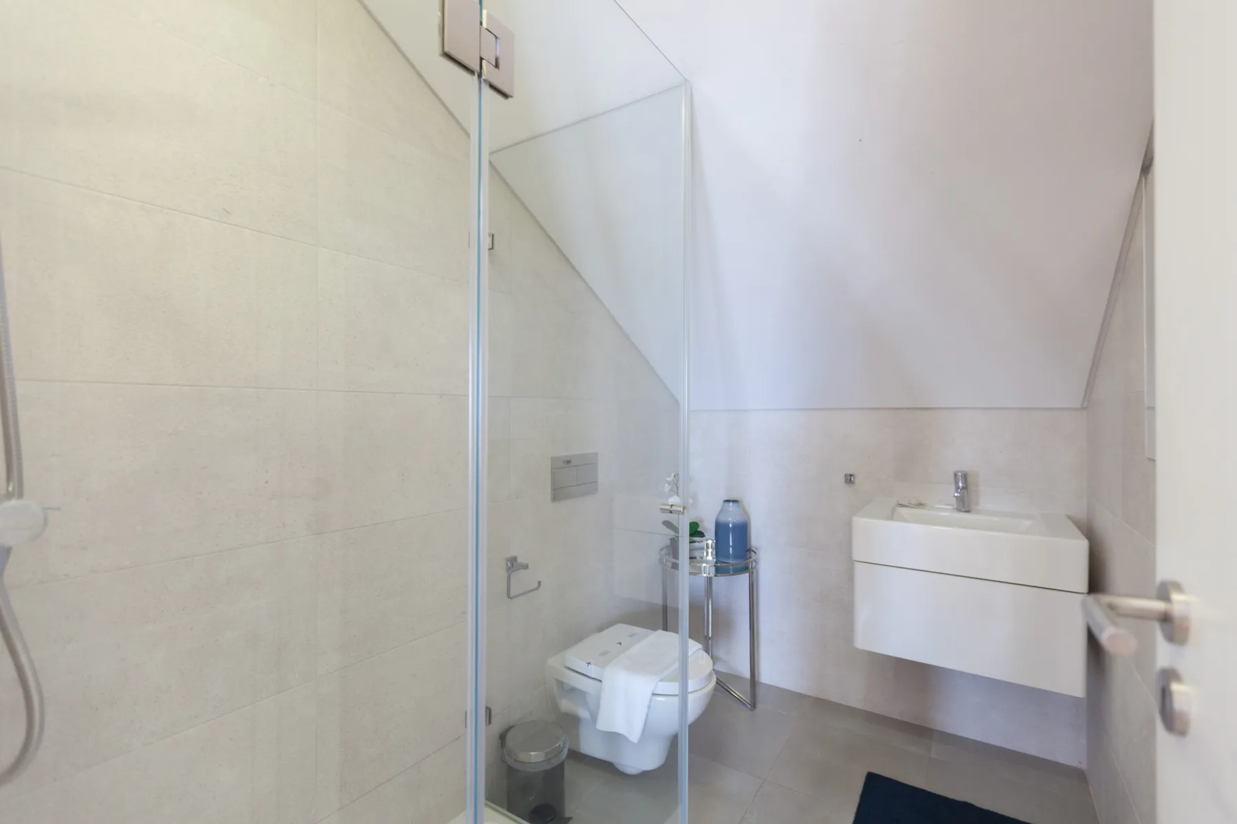 A bathroom with a glass shower, toilet, and wall-mounted sink.