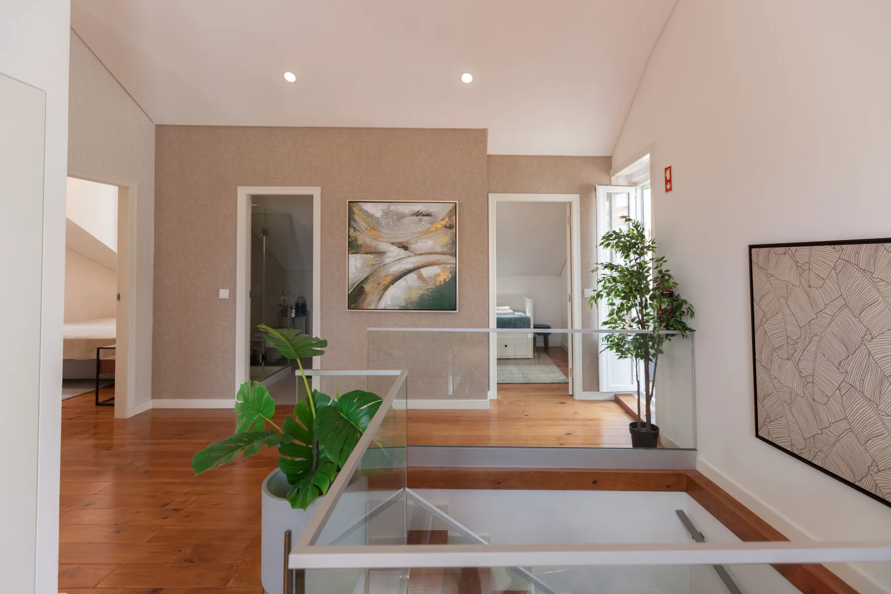 A bright interior hallway opens onto a glass-railed stairwell, with artwork on the walls.