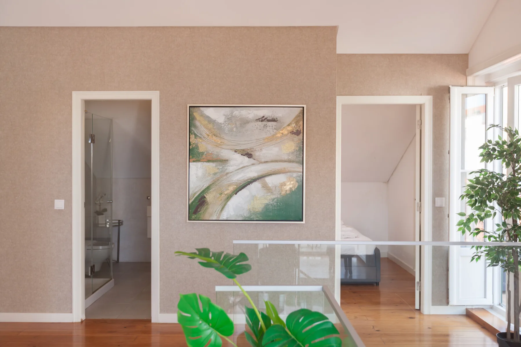 Interior hallway with a glass railing, framed artwork, and an open doorway.