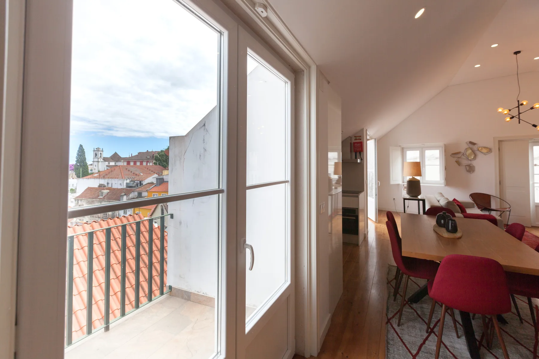 A bright dining area opens onto a small balcony with city rooftops beyond.