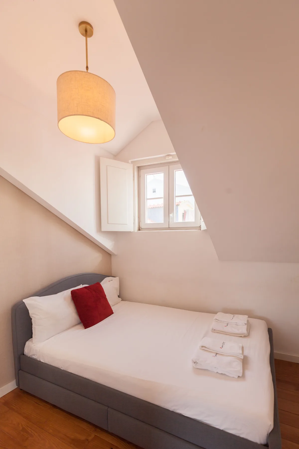 A bedroom with a bed, folded towels, and a small window.