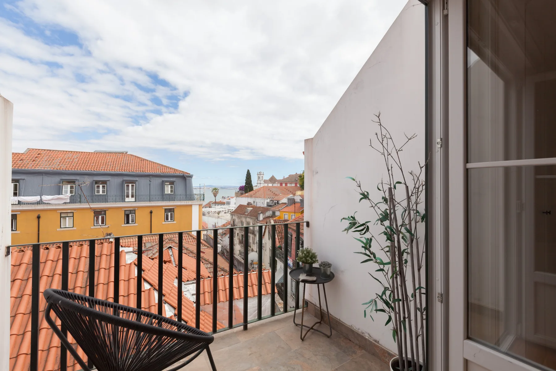 A balcony with seating and potted plants overlooks nearby rooftops.