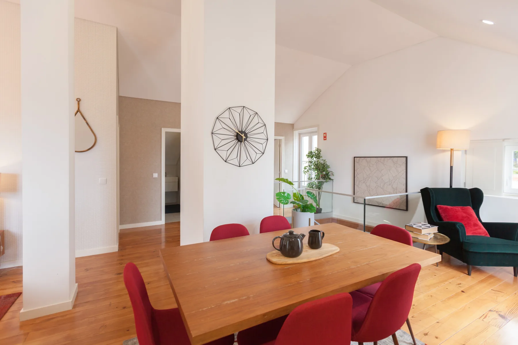 A dining and living area with a wooden table, red seating, and a dark armchair.