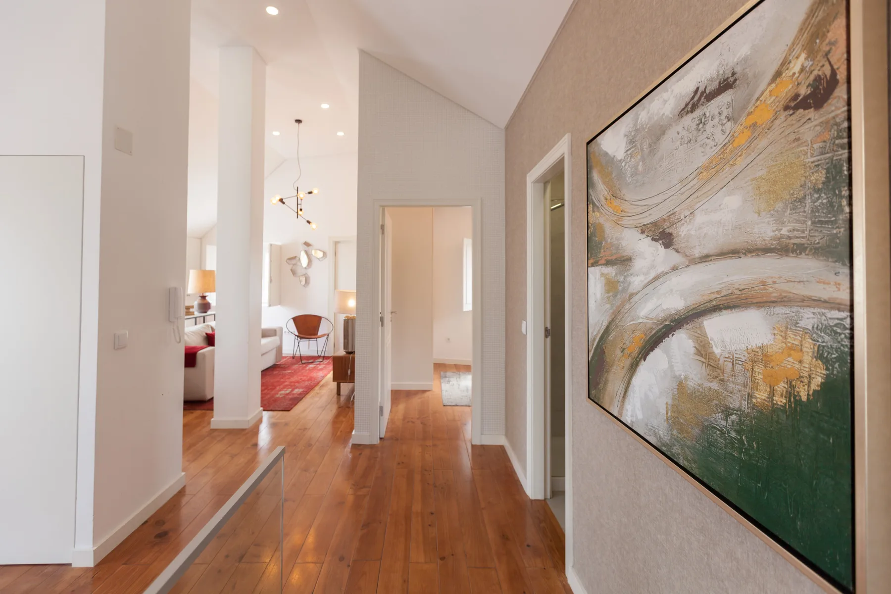 A bright apartment hallway opens toward a living area, with wood flooring and large abstract artwork.
