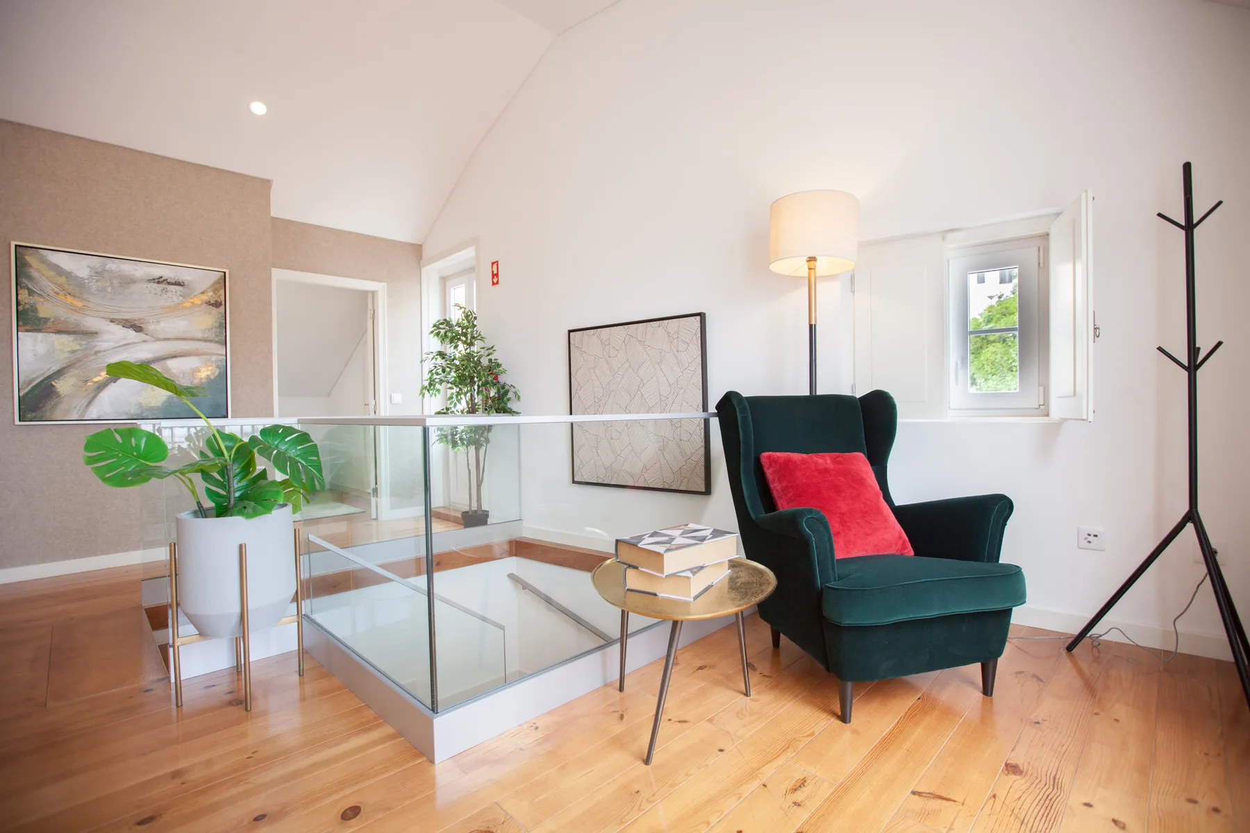 A bright living area with a dark armchair beside a glass-railed stair opening.