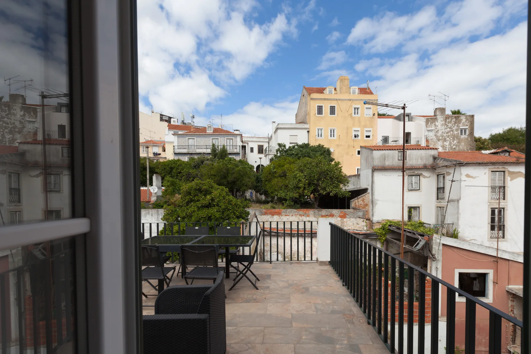 A terrace overlooks nearby buildings and trees beneath a partly cloudy sky.