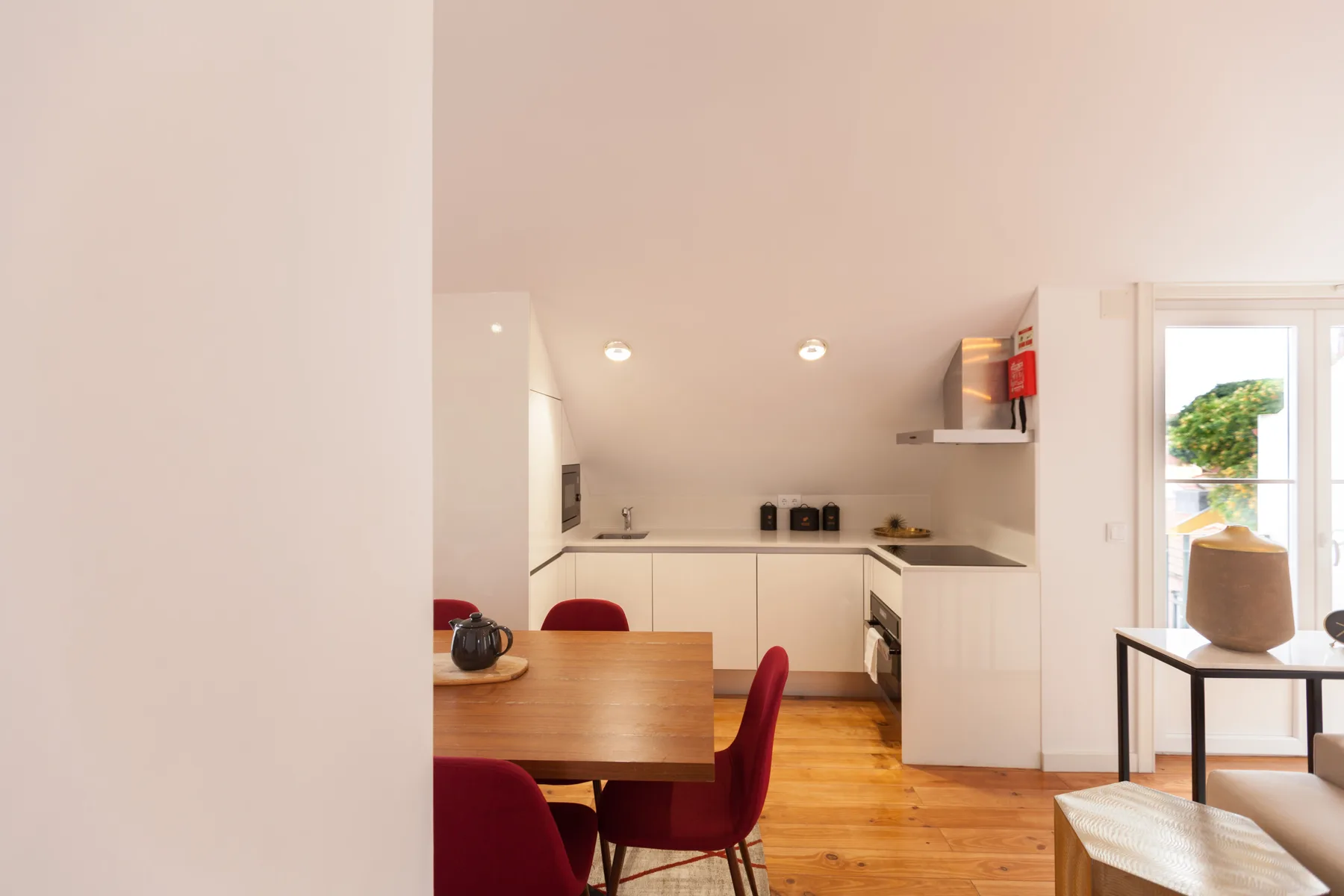A dining area with a wooden table and red seating beside a compact kitchen.
