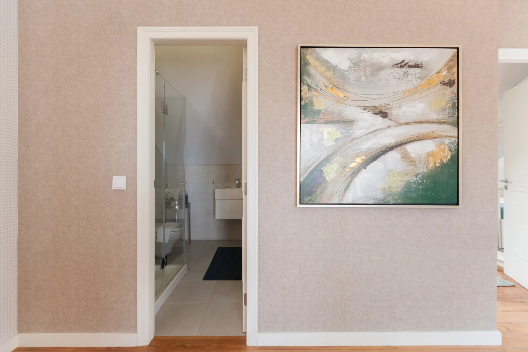 A hallway wall with an abstract painting and an open bathroom doorway.