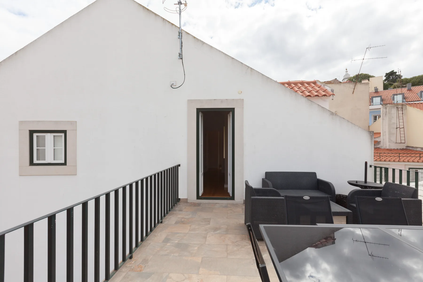 A rooftop terrace with dark seating, a tiled floor, and a doorway.