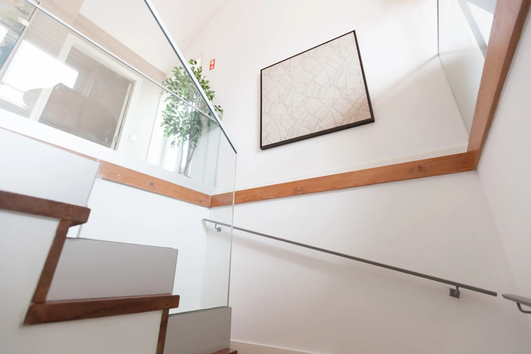 A bright stairwell with a glass railing and framed artwork on the wall.