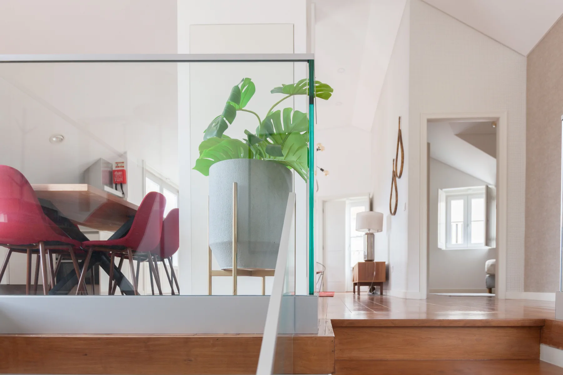 A bright dining area with red seating sits beside a glass partition and potted plant.