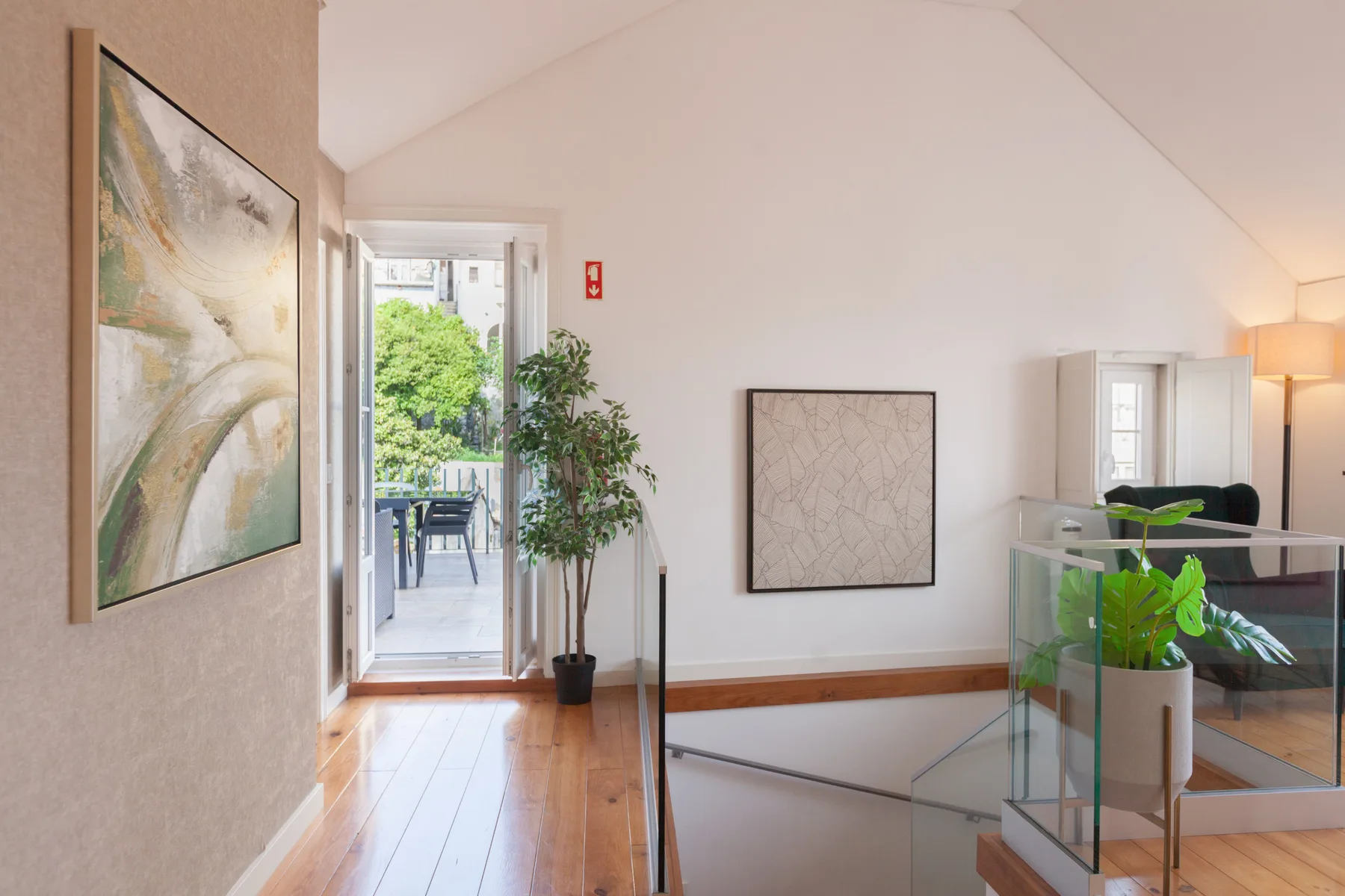 A bright interior landing opens onto a balcony with outdoor seating and leafy plants.