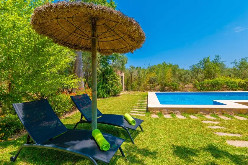 A garden pool area with reclining loungers beneath a thatched parasol.