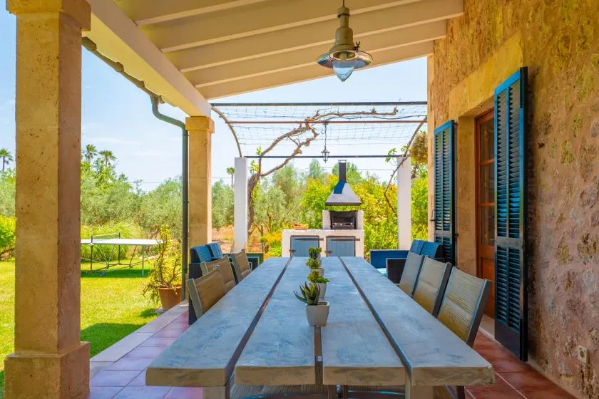 A covered outdoor dining area with a long table overlooking a garden.