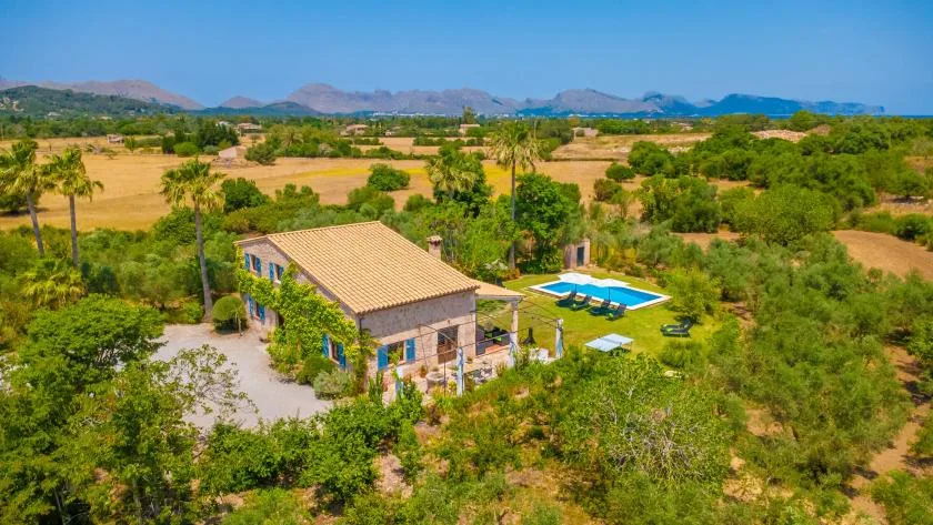 A rural home with a swimming pool sits among trees and open fields.