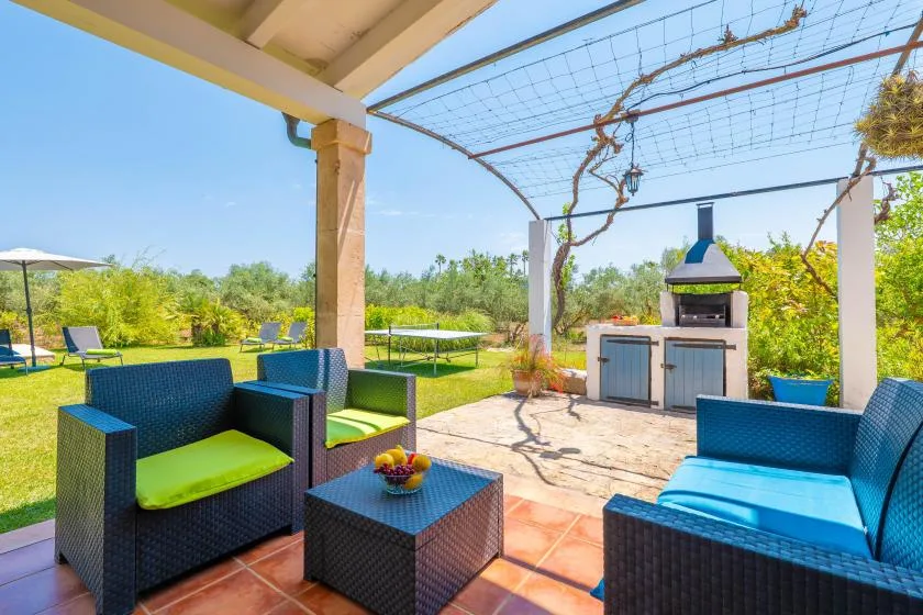 A covered outdoor patio has wicker seating, a table, and a built-in grill.