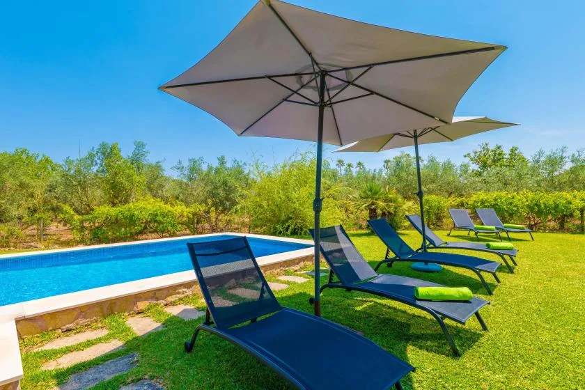 Outdoor poolside seating beneath large umbrellas on a sunny lawn.