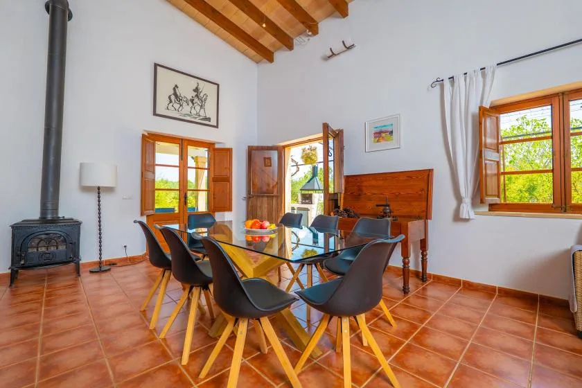 A dining area with a glass-top table and chairs beneath exposed wooden ceiling beams.
