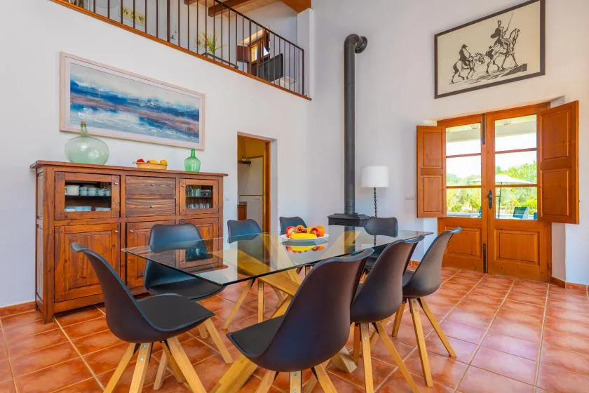 A dining area with a glass table and dark seating beneath a loft railing.