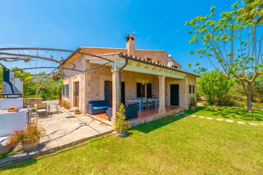 A stone house opens onto a sunny patio beside a green lawn.