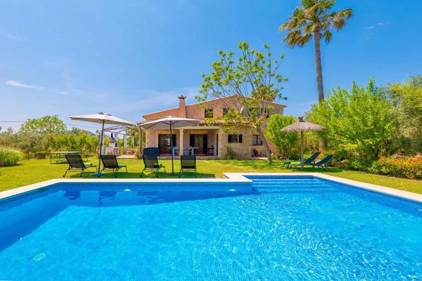 A swimming pool sits in front of a house, with lounge seating on the lawn.