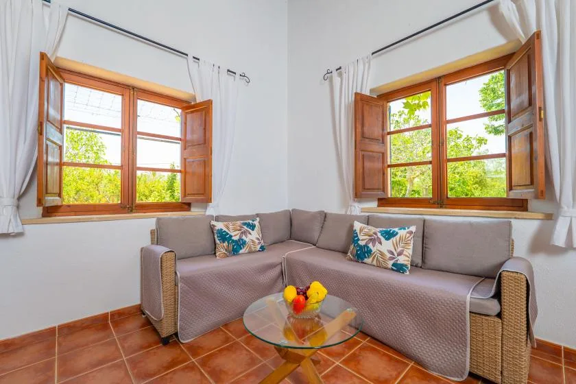 A living room with corner seating beneath two open windows.