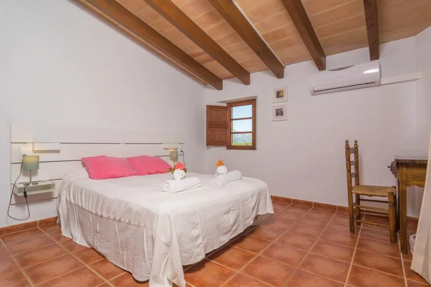 A bedroom with a double bed, pink pillows, and exposed wooden ceiling beams.