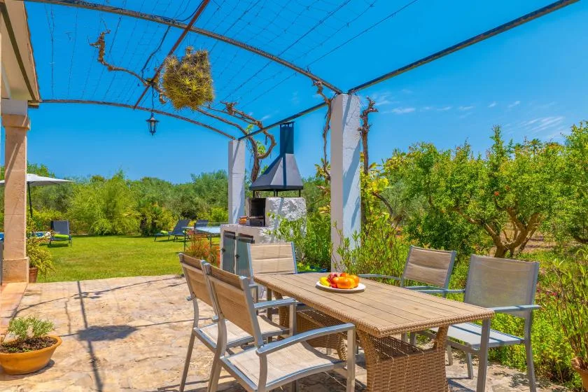 An outdoor patio dining area sits beneath a pergola, with garden greenery beyond.