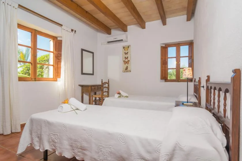 A bright bedroom with white-covered beds and wooden ceiling beams.